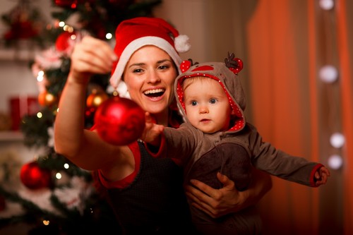 Happy mother showing Christmas ball  to baby near Christmas tree