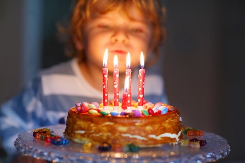 Adorable four year old kid celebrating his birthday and blowing candles on homemade baked cake, indoor. Birthday party for kids. Focus on child