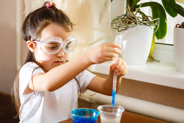 Little girl experimenting in elementary science class with protective gloves and glasses